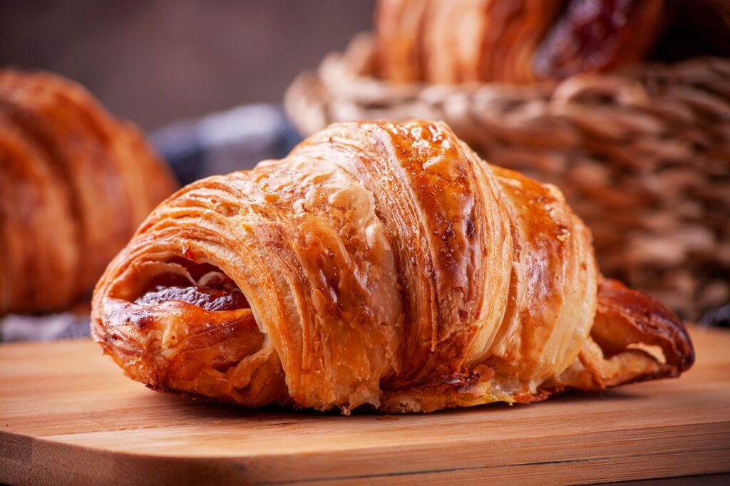 Close-up of a golden, flaky croissant on a wooden board, perfect for breakfast visuals.